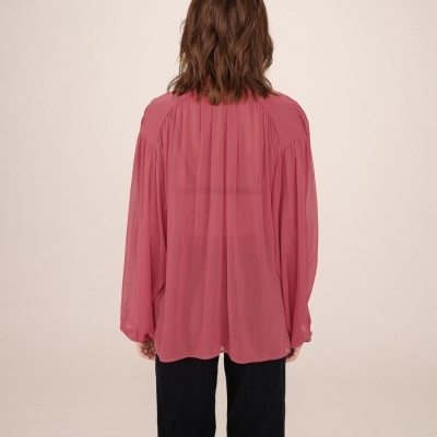 Camisa rosa feminina de tecido leve e transparente vista de costas com calças pretas