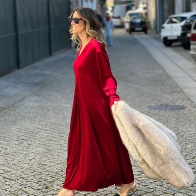 Mulher com vestido longo vermelho, sapatos bege com biqueira preta e casaco peludo bege, caminhando na rua de calçada.