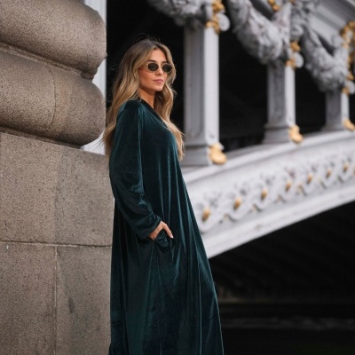 Mulher a usar vestido verde-escuro de veludo e botas castanhas, em rua com arquitetura clássica