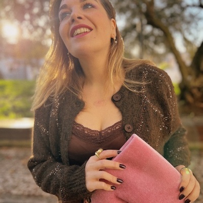 Mulher sorridente com camisola castanha e bota rosa felpuda ao ar livre.