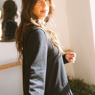 Mulher com jersey preto e saia plissada em interior luminoso com planta