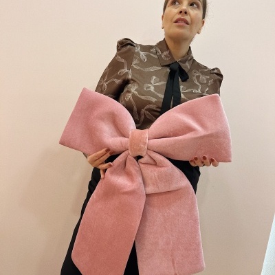 Mulher segura grande laço cor-de-rosa aveludado com blusa castanha e padrão floral.