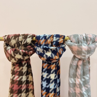 Três cachecóis coloridos com padrão pied-de-poule pendurados num varão amarelo