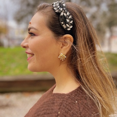 Mulher com bandolete preta decorada e brincos dourados com pérolas