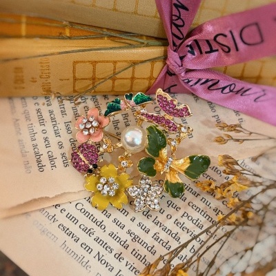 Broche floral com esmalte colorido, cristais e pérola artificial sobre páginas de livro e flores secas