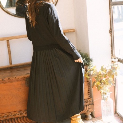 Mulher a usar saia plissada preta e botas castanhas em ambiente interior iluminado pelo sol.