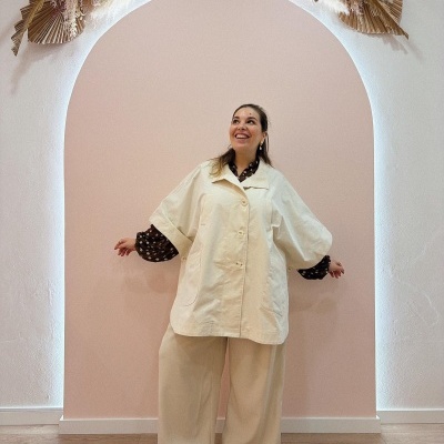 Mulher a usar casaco e calças creme com camisa castanha de bolinhas em interior decorado