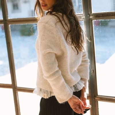 Mulher a usar cardigan bege e saia preta de malha junto a uma janela de moldura metálica