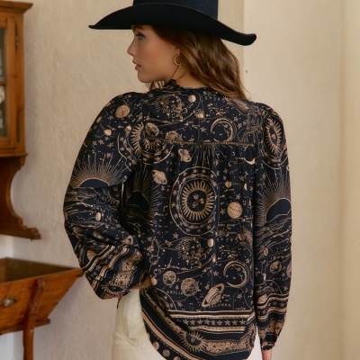 Blusa preta com padrão de mapas celestes bege e calças claras, chapéu preto em interior