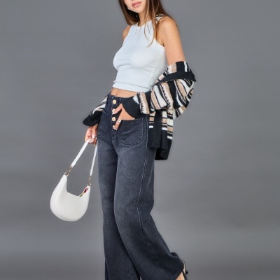 Mulher com top branco, casaco às riscas, calças largas de ganga cinza e mala branca