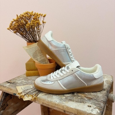 Ténis em camurça branca e tecido prateado sobre banco de madeira com flores secas e papel