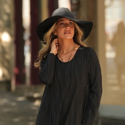 Mulher com vestido preto e chapéu preto largo em ambiente urbano