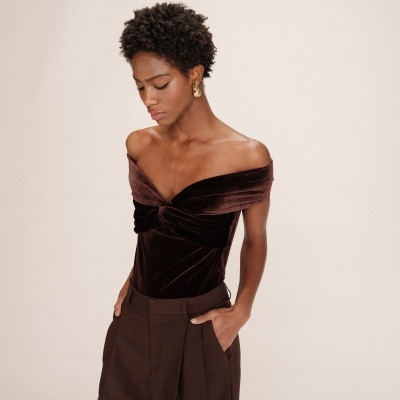 Mulher com top castanho de veludo ombro a ombro e calças castanhas largas com pregas.