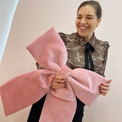 Mulher sorridente segurando laço cor de rosa grande aveludado