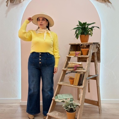 Mulher com camisola amarela e jeans ao lado de escadote de madeira com plantas e livros