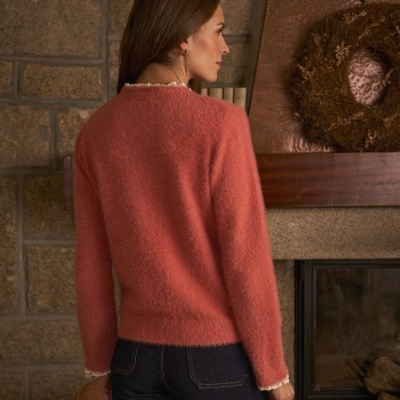 Mulher de costas com camisola de malha cor de rosa e calças de ganga junto a lareira