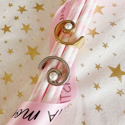 Dois anéis espiral dourado e prateado com pérolas sobre palhinhas rosa e brancas e fita rosa