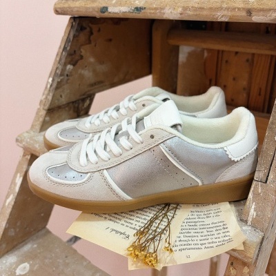 Ténis brancos com detalhe prateado sobre escada de madeira com papel e flores secas