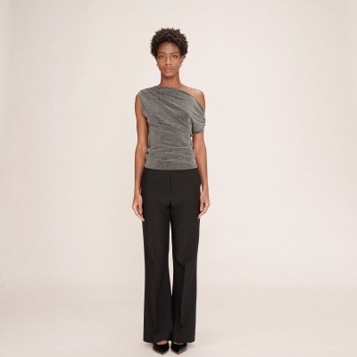 Mulher com top cinza metálico assimétrico e calças pretas em fundo neutro