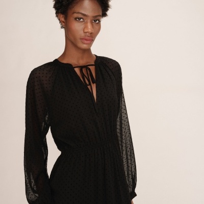 Vestido preto de tecido transparente com padrão de pequenos pontos e laço no decote