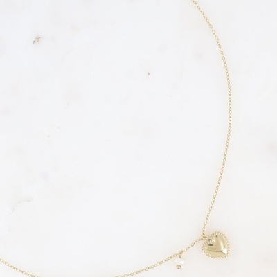 Colar dourado com pendente de coração e pérola sobre superfície branca