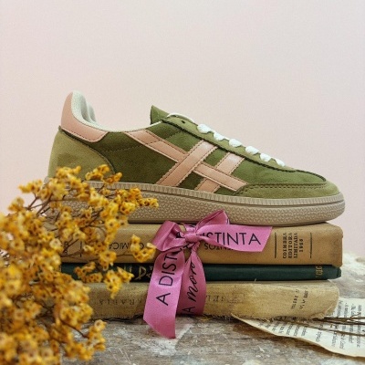 Ténis camurça verde com detalhes rosa sobre livros antigos e fita rosa