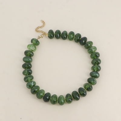 Colar de contas verdes translúcidas com fecho dourado sobre fundo bege