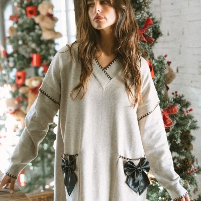 Vestido cinza claro de malha com laços pretos nos bolsos e decoração natalícia ao fundo