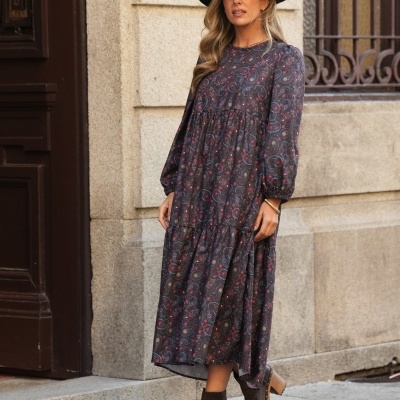 Mulher com vestido comprido estampado, chapéu preto e botas castanhas na rua