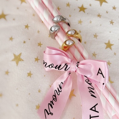 Anéis com pérolas em canudos rosas com laço e fundo de estrelas douradas