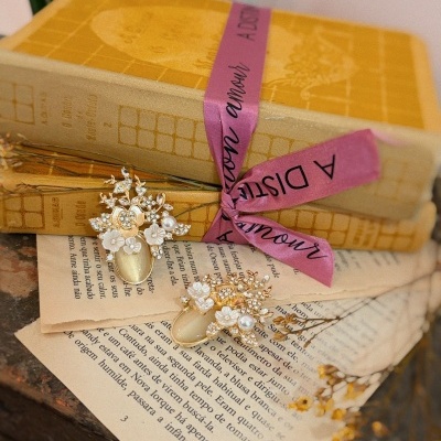 Livros antigos amarelos com fita rosa e brincos dourados com pedras e pérolas