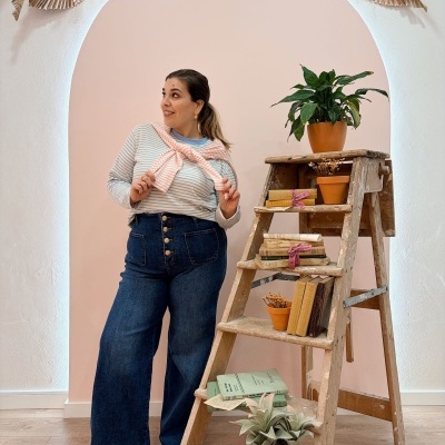 Mulher com camisola riscada rosa e jeans ao lado de escadote com plantas e livros