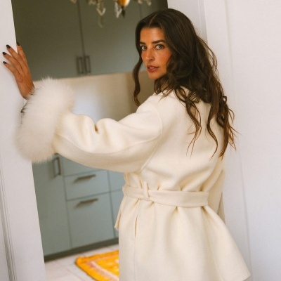 Casaco feminino branco com cinto e punhos de pelo branco num ambiente interior