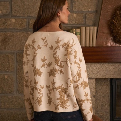 Mulher de costas usando suéter bege com padrão floral bordado em ambiente rústico