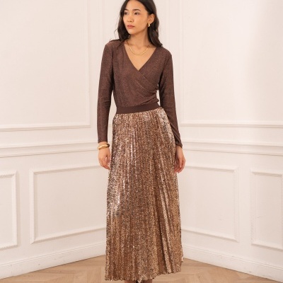 Mulher com blusa castanha brilhante e saia dourada plissada com lantejoulas