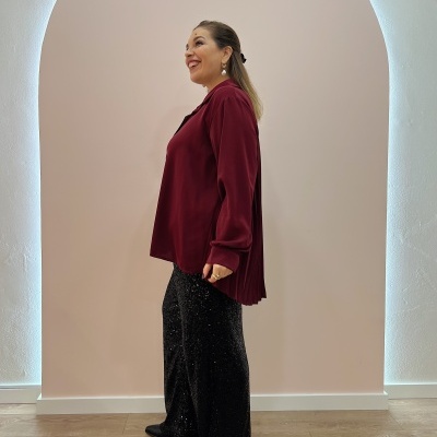 Mulher com blusa bordô e calças pretas brilhantes em fundo bege com arco iluminado