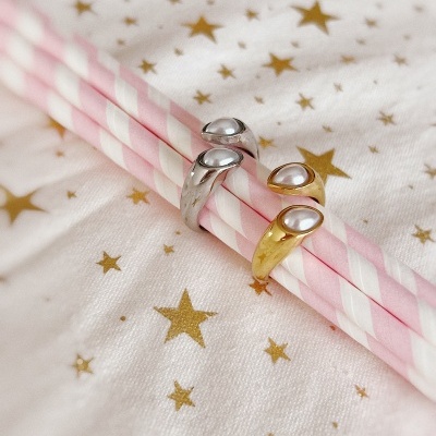 Anéis dourado e prateado com pérolas sobre palhinhas cor-de-rosa e tecido branco com estrelas douradas