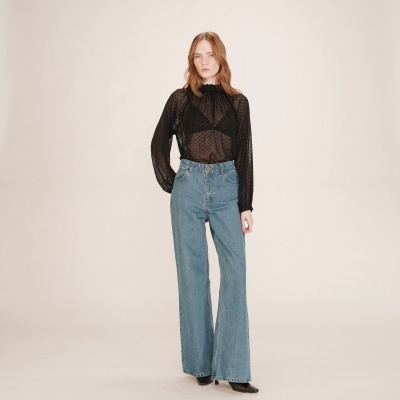 Mulher vestindo blusa preta transparente de mangas compridas e calças de ganga largas azuis