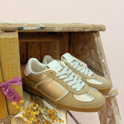 Ténis bege e creme com sola castanha sobre escada de madeira junto a livros e flores secas