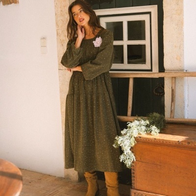 Vestido comprido verde-oliva com padrão discreto e flor rosa claro decorativa.