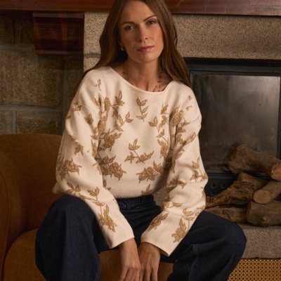 Mulher com camisola branca bordada sentada num sofá castanho junto a lareira
