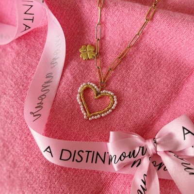 Colar dourado com pendente de coração e trevo sobre fundo rosa com fita de texto