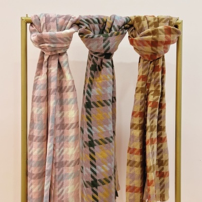 Três cachecóis xadrez coloridos pendurados num suporte metálico dourado