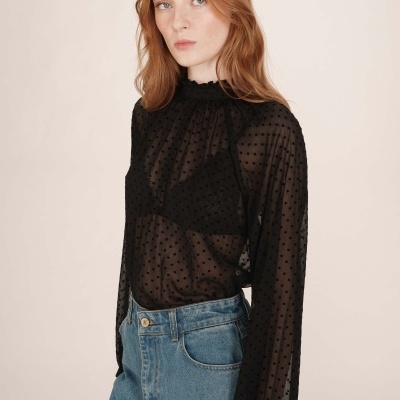 Mulher com blusa preta transparente de bolinhas e jeans azul claro