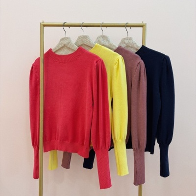 Quatro camisolas de malha coloridas penduradas numa estrutura metálica dourada