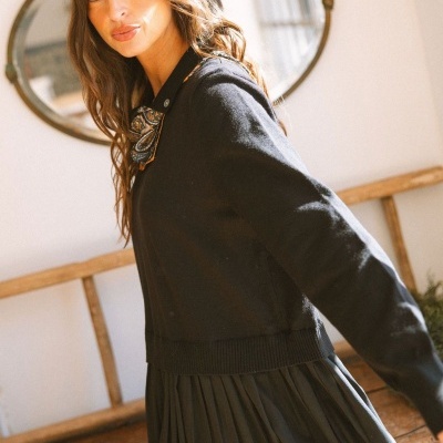 Mulher com camisola e saia preta e lenço estampado, em ambiente interior com espelho oval ao fundo