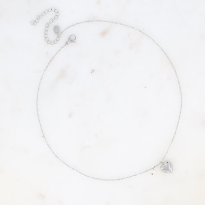 Colar prateado com pendente de coração em fundo branco marmoreado