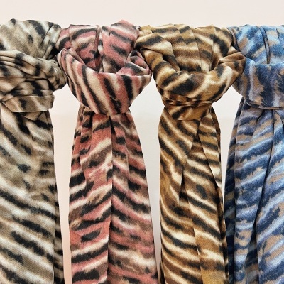 Quatro lenços de tecido com padrão animal em diferentes cores: bege, rosa, castanho e azul.