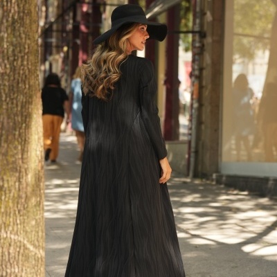 Mulher com vestido longo preto e chapéu preto a caminhar numa rua urbana