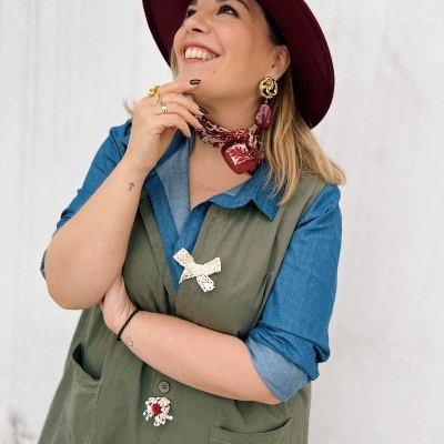 Mulher com camisa azul e colete verde com aplicações florais e chapéu bordô